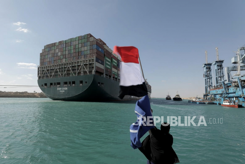  Sebuah foto selebaran yang disediakan oleh Otoritas Terusan Suez menunjukkan seorang Mesir mengibarkan bendera Mesir di dekat kapal kontainer Ever Given setelah diapungkan kembali di Terusan Suez, Mesir, 29 Maret 2021. Pada 17 November 1869 Terusan Suez yang hubungkan Laut Tengah dan Merah diresmikan.