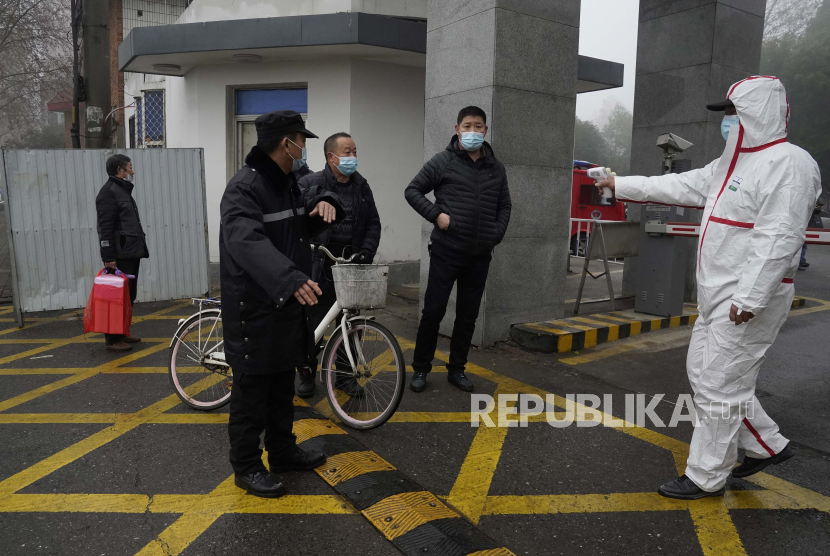 Seorang pekerja dengan alat pelindung memegang termometer di pintu masuk ke Pusat Pengendalian dan Pencegahan Penyakit Hubei di mana tim Organisasi Kesehatan Dunia melakukan kunjungan lapangan di Wuhan di provinsi Hubei China tengah, Senin (1/2/2021). Misi WHO tim yang menyelidiki asal-usul pandemi virus korona di Wuhan.