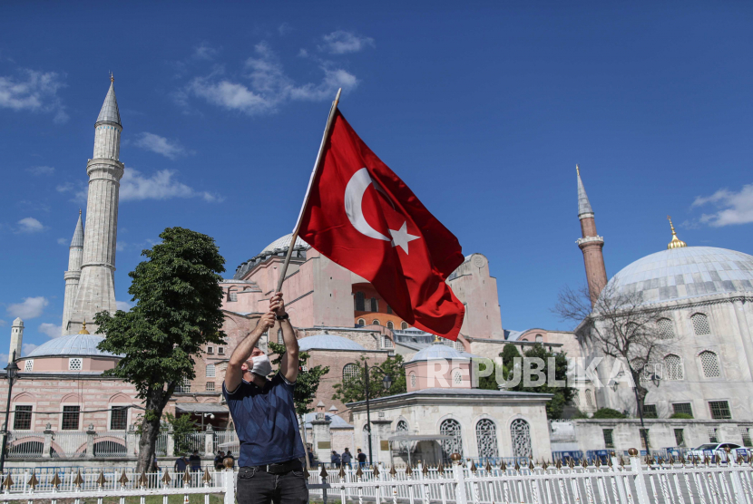 Seorang pria memegang bendera Turki di depan Museum Hagia Sophia di Istanbul, Turki