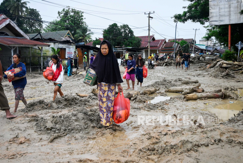 Orang-orang membawa barang-barang mereka saat berjalan di jalan berlumpur setelah banjir bandang di Masamba, Sulawesi Selatan, Indonesia, 15 Juli 2020. Menurut Badan Nasional Penanggulangan Bencana Indonesia (BNPB), setidaknya 15 orang tewas dan puluhan yang lain dilaporkan hilang setelah banjir parah melanda Sulawesi Selatan pada 14 Juli.
