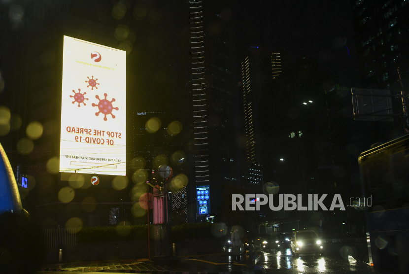 Seorang warga melintasi papan himbauan terkait virus corona atau COVID-19 di Jalan Sudirman Jakarta, Senin (30/3/2020). Presiden meminta penerapan  pembatasan sosial berskala besar, physical distancing dilakukan lebih tegas, lebih disiplin dan lebih efektif untuk menekan penyebaran COVID-19