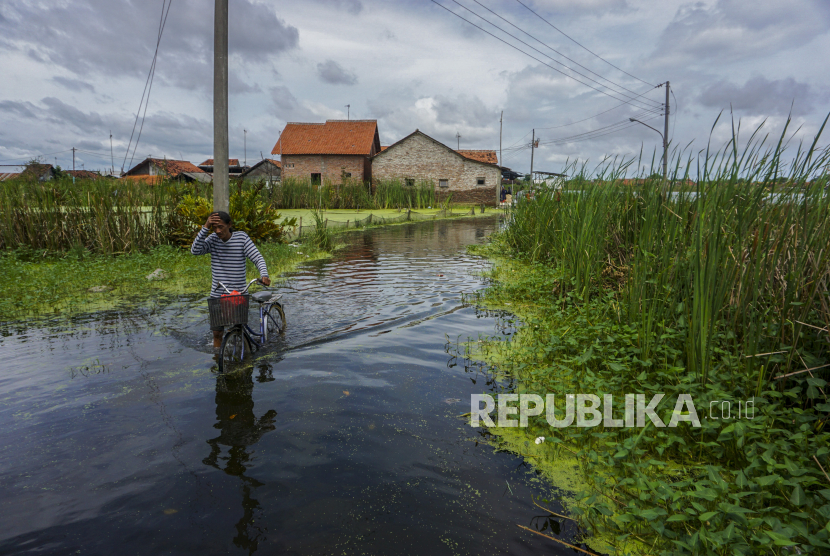 Warga mendorong sepedanya melewati genangan banjir. 
