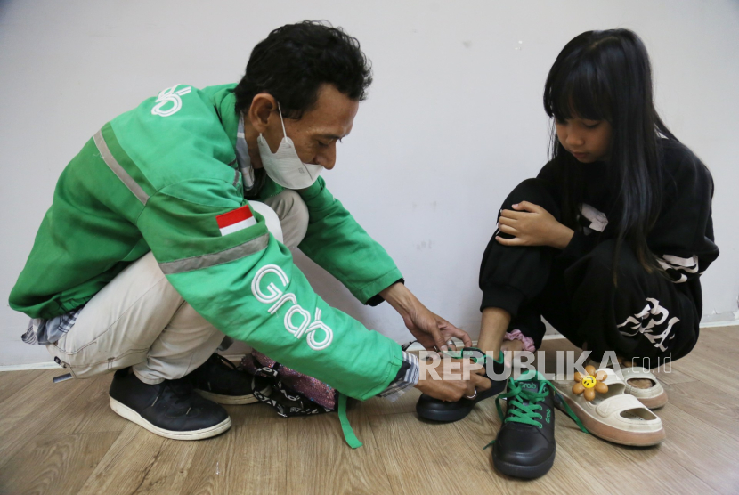 Mitra pengemudi Grab memakaikan sepatu kepada anaknya saat penyerahan bantuan sepatu dari Grab Indonesia di Jakarta (ilustrasi).