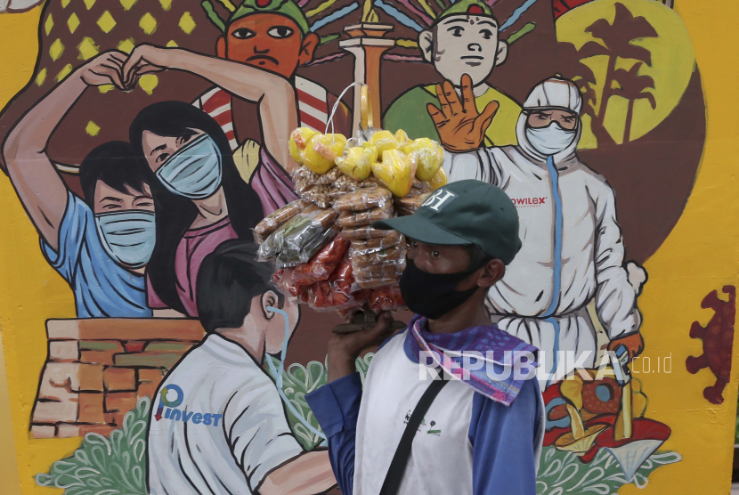 Seorang penjual makanan berjalan melewati mural bertema coronavirus di Jakarta, Indonesia, Selasa, 15 Desember 2020. Indonesia telah melaporkan lebih banyak kasus virus corona daripada negara lain di Asia Tenggara.