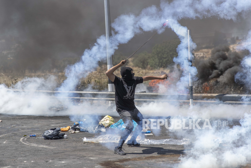 Seorang demonstran Palestina menggunakan katapel untuk mengembalikan tabung gas air mata ke arah tentara selama bentrokan dengan pasukan Israel di pintu masuk utara kota Ramallah, Tepi Barat, Selasa, 18 Mei 2021.