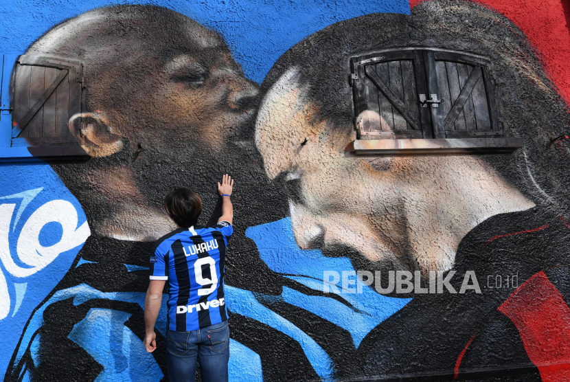 Seorang pendukung Inter menyentuh mural di dekat Stadion Giuseppe Meazza, yang menggambarkan Romelu Lukaku (kiri) dari Inter Milan dan Zlatan Ibrahimovic dari AC Milan bertengkar saat pertandingan derbi Milan, 15 Februari 2021. 
