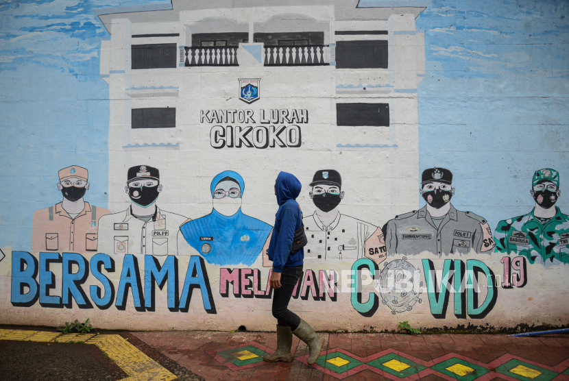 Warga berjalan melintasi mural bertemakan Covid-19 di kawasan Cawang, Jakarta.