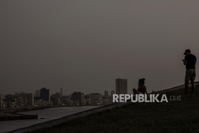 Dua orang menikmati matahari terbenam disaat awan debu Sahara menyelimuti udara di Havana, Rabu (24/6).Foto AP / Ramon Espinosa