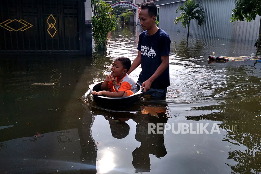 Warga bersama anaknya menerobos banjir di Kelurahan Trimulyo, Genuk, Kota Semarang, Jawa Tengah, Selasa (3/12/2023). 