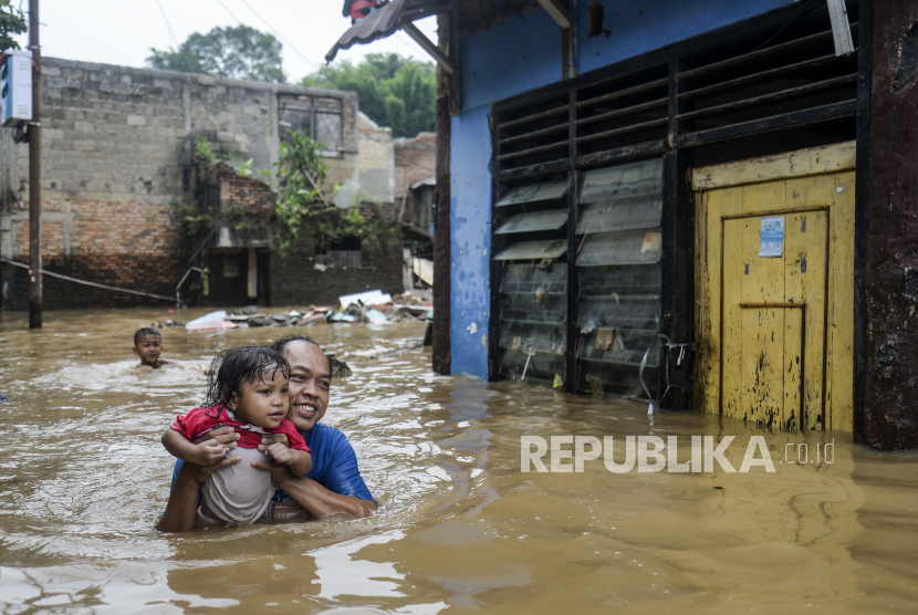 Warga berjalan menggendong anaknya saat terjadi banjir di kawasan Rawajati, Jakarta, Senin (10/10/2022). Pemkot Jakbar membuka layanan untuk memperbaiki dokumen rusak akibat banjir.
