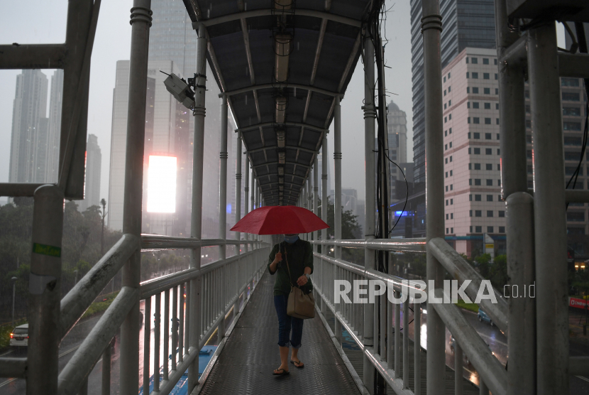 Seorang warga membawa payung saat melintas di jembatan penyeberangan orang (JPO) di Jalan Jenderal Sudirman, Jakarta, Jumat (16/10/2020). Badan Meteorologi Klimatologi dan Geofisika (BMKG) memprakirakan sejumlah wilayah DKI Jakarta akan diguyur hujan disertai petir pada siang hari sepanjang Rabu (2/12).