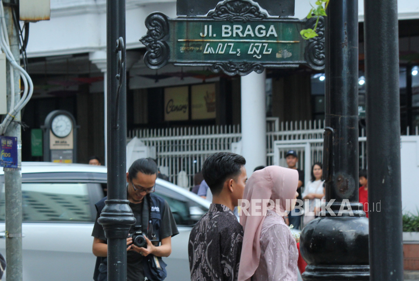 Pengunjung berfoto bersama fotografer jalanan di kawasan Jalan Braga, Kota Bandung, Jumat (30/6/2023). Kawasan Braga merupakan salah satu destinasi wisata wajib bagi pengunjung yang datang ke Kota Bandung, khususnya saat musim liburan. Lebih dari sekedar berbelanja dan menikmati cafe, di jalan penuh sejarah itu, pengunjung bisa menghabisakan waktu berjam- jam untuk berfoto. Saat ini, selain berswafoto pengunjung juga bisa menggunakan jasa fotografer jalanan dengan tarif Rp 5.000 per foto dengan kualitas kamera profesional.