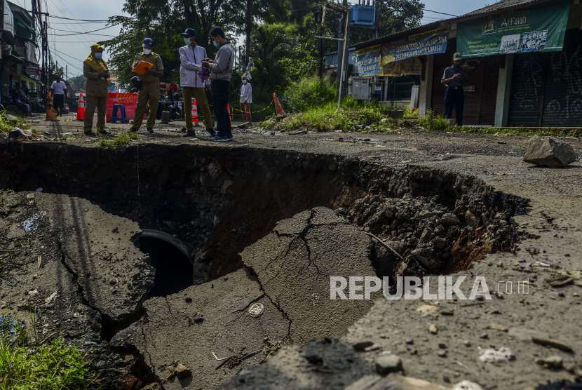 Petugas berdiri di dekat jalan yang longsor di Kampung Setu Asem, Mekarwangi, Tanah Sareal, Kota Bogor, Senin (10/5). Jalan yang longsor akibat hujan dengan intensitas deras dan tergerusnya pondasi tanah oleh aliran Kali Cigede Kulon. Bencana tersebut mengancam keselamatan tiga unit rumah warga hingga membuat jalan harus ditutup dari lalu lintas kendaraan. Republika/Putra M. Akbar