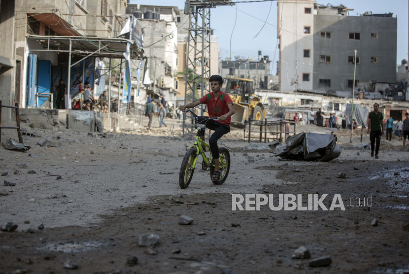 Seorang anak laki-laki Palestina mengendarai sepeda di tengah rumah dan toko yang rusak menyusul serangan udara Israel di kamp pengungsi Jabaliya, Jalur Gaza utara, Kamis, 20 Mei 2021. 
