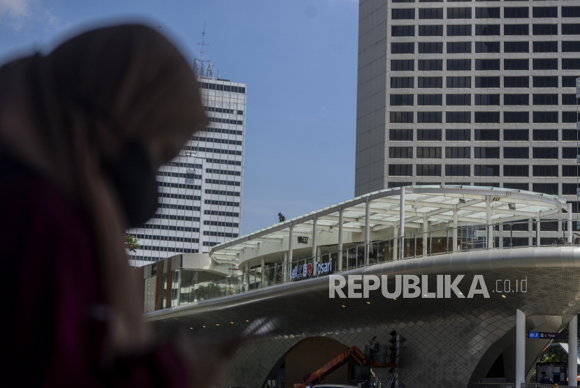 Warga menggunakan masker menunggu waktu menyeberang di Jalan Jenderal Sudirman, Jakarta.