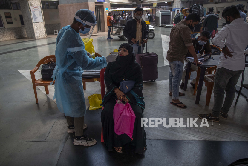  Seorang petugas kesehatan mengumpulkan sampel swab dari seorang pelancong di stasiun kereta api untuk menguji COVID-19, sebelum dia diizinkan masuk ke kota itu, di Mumbai, Rabu, 5 Januari 2022. Negara bagian terkaya di India membuka kembali kelas tatap muka.