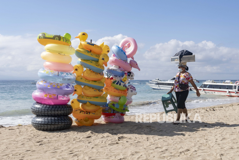 Seorang penjual makanan mendekati cincin renang tiup yang disusun dalam tumpukan saat dia berjalan di pantai yang hampir kosong di Sanur, Bali, Indonesia, 09 Juni 2021. Pemerintah Indonesia telah merencanakan untuk membuka kembali pulau resor Bali untuk turis asing pada akhir Juli 2021. 
