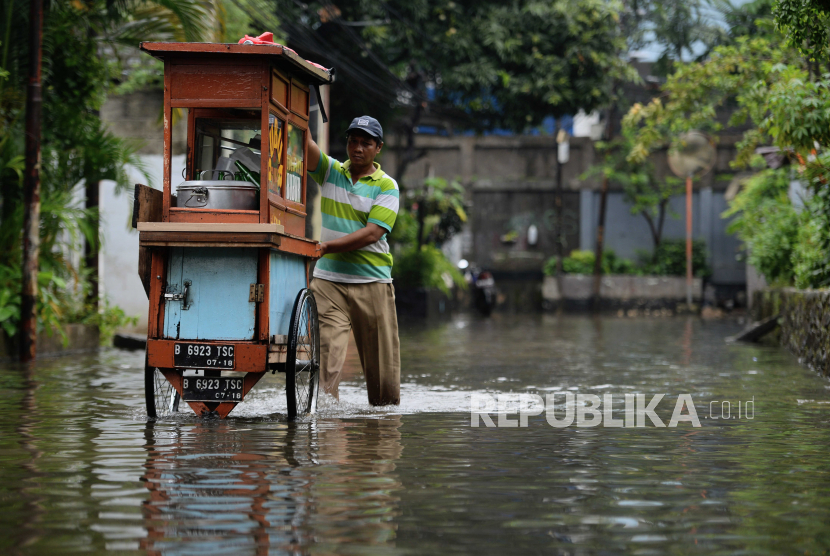 Pedagang mendorong gerobaknya saat banjir di kawasan Petogogan, Jakarta, Jumat (24/2/2023). Banjir setinggi  40 sentimeter di kawasan pemukiman warga tersebut dipicu luapan air dari Kali Krukut akibat hujan deras yang mengguyur Jakarta sejak dini hari.