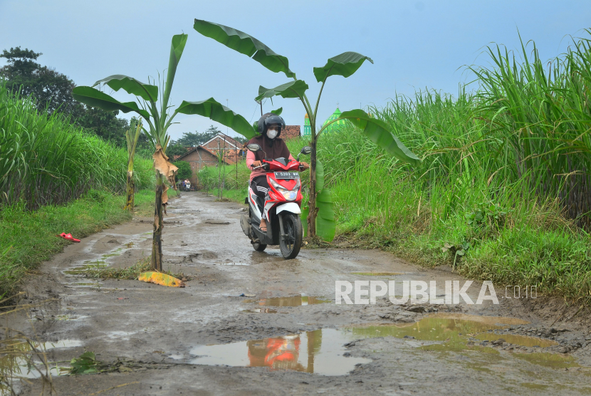 Pengendara sepeda motor melintasi jalan rusak yang ditanami pohon pisang (ilustrasi)