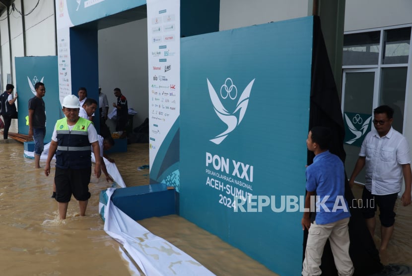 Sejumlah pekerja berusaha menghalau aliran air agar tidak masuk ke venue lapangan tembak indoor SR 50 meter PON XXI Aceh-Sumut 2024 di Lapangan Tembak Rindam IM Mata Ie, Aceh Besar, Aceh, Selasa (17/9/2024). Sejumlah area di venue menembak tersebut tergenang air akibat hujan dengan intensitas tinggi. 