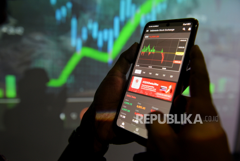 Pengunjung mengamati data saham melalui aplikasi IDX Mobile di dekat layar yang menampilkan indeks harga saham gabungan (IHSG).