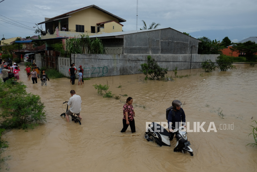 Warga melintasi banjir yang merendam pemukiman penduduk di Kecamatan Sunggal, Deli Serdang, Sumatera Utara, Jumat (4/12/2020). Banjir akibat meluapnya daerah aliran sungai Belawan menyebabkan ribuan rumah warga terendam. 