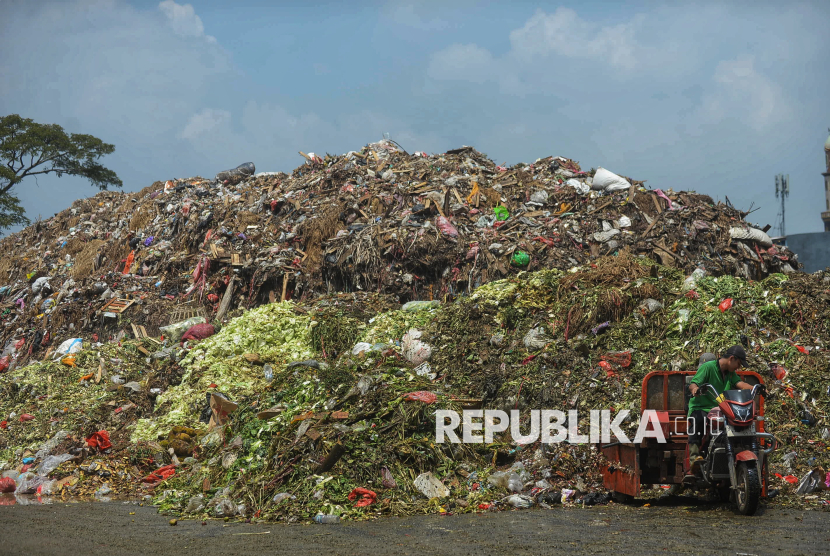 Pekerja beraktivitas di dekat tumpukan sampah di Pasar Induk Kramat Jati, Jakarta, Rabu (1/4/2026). Hingga saat ini, kondisi sampah masih tampak menggunung dengan ketinggian yang mencapai sekitar enam meter.  Tumpukan sampah tersebut didominasi oleh sampah sayuran dan buah.  Berdasarkan pantauan Republika di lokasi sejak pukul 10.45 hingga 11.45 WIB, belum terlihat adanya truk yang mengangkut sampah untuk dibuang ke lokasi pengolahan selanjutnya maupun ke TPST Bantargebang. Sejumlah pedagang mengeluhkan kondisi tersebut karena dinilai mengganggu aktivitas dan kenyamanan di area pasar.