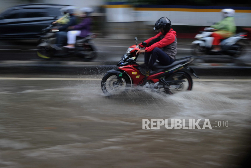 Pengendara motor melewati genangan air saat hujan deras (ilustrasi)