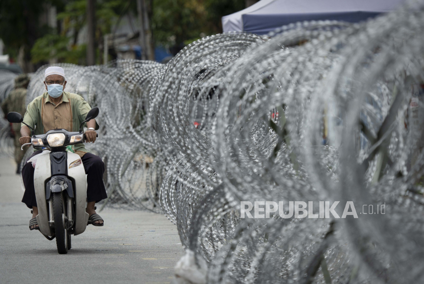 Pengendara sepeda motor berjalan sepanjang pagar kawat berduri di area lockdown Selayang Baru, di luar Kuala Lumpur, Malaysia, Ahad (26/4). (ilustrasi)