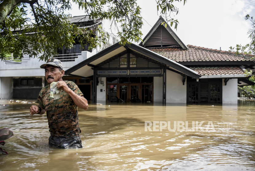 Seorang warga beraktivitas di halaman rumah yang terendam air saat banjir melanda (ilustrasi)