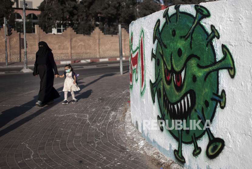  Seorang wanita Palestina berjalan bersama putrinya di samping mural yang menggambarkan virus corona, di Kota Gaza, Senin, 14 September 2020. 