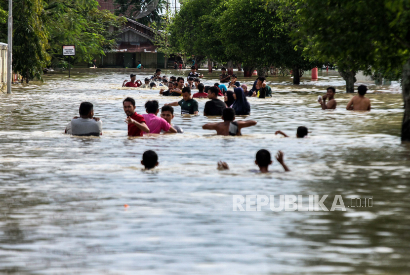 Sejumlah warga mengarungi banjir yang merendam ibukota Lhoksukon, Aceh Utara, Aceh, Senin (7/12/2020). Pemerintah Kabupaten Aceh Utara menetapkan status tanggap darurat bencana banjir yang melanda 22 kecamatan dan menerapkan status siaga 1 bencana daerah selama 14 hari terhitung 7 Desember 2020 hingga 20 Desember 2020