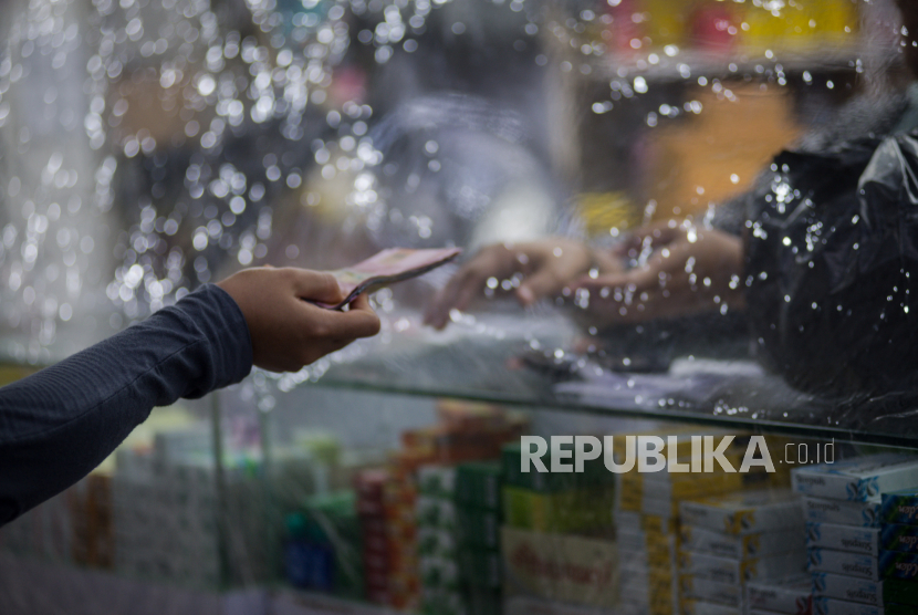 Pekerja melayani pembeli dari balik plastik pembatas di Apotek  kawasan Pasar Baru, Jakarta, Jumat (3/4). Penggunaan plastik pembatas tersebut bertujuan untuk mengantisipasi penyebaran virus corona atau COVID-19
