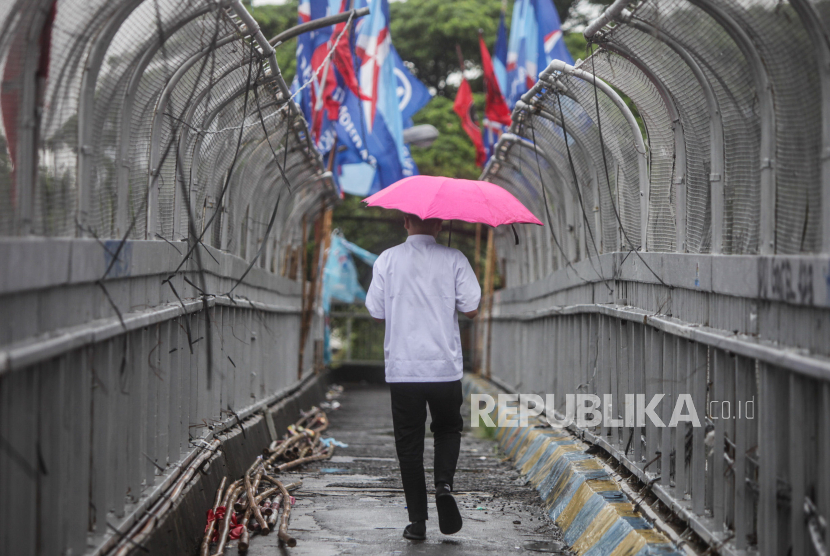 Warga memakai payung saat hujan turun di Jalan Gatot Subroto, Jakarta Selatan, Jumat (19/1/2024). 