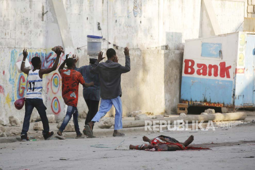 Warga berjalan melewati jenazah pria saat bentrokan antara polisi dan anggota geng di lingkungan Portail di Port-au-Prince di Port-au-Prince, Haiti, Kamis, (29/2/2024).