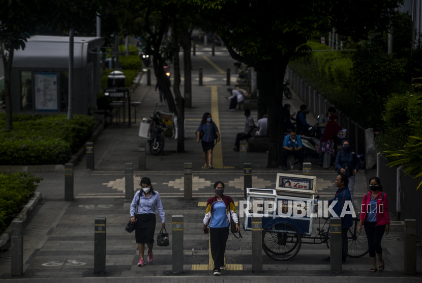 Sejumlah pekerja melintasi trotoar di kawasan Sudirman, Jakarta.