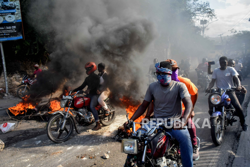 Pengunjuk rasa mengendarai sepeda motor melewati tumpukan sampah yang terbakar saat demonstrasi di Port-au-Prince, Haiti, (6/2/2024).