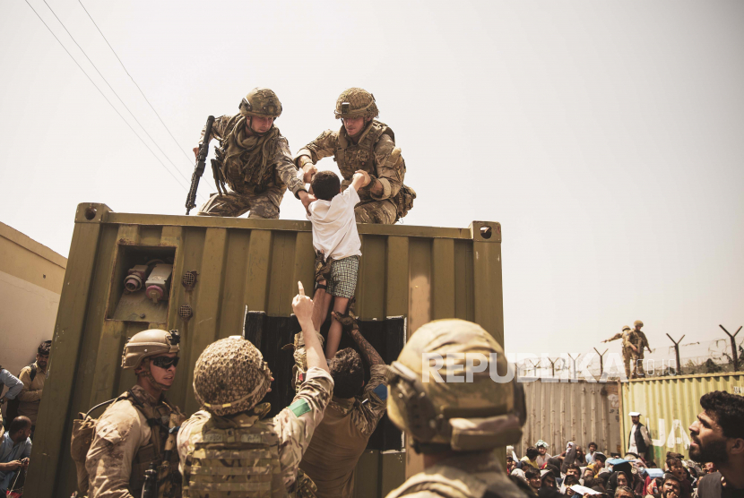 Dalam gambar yang disediakan oleh Korps Marinir AS, pasukan koalisi Inggris dan Turki, bersama dengan Marinir AS, membantu seorang anak selama evakuasi di Bandara Internasional Hamid Karzai di Kabul, Afghanistan, Jumat, 20 Agustus 2021