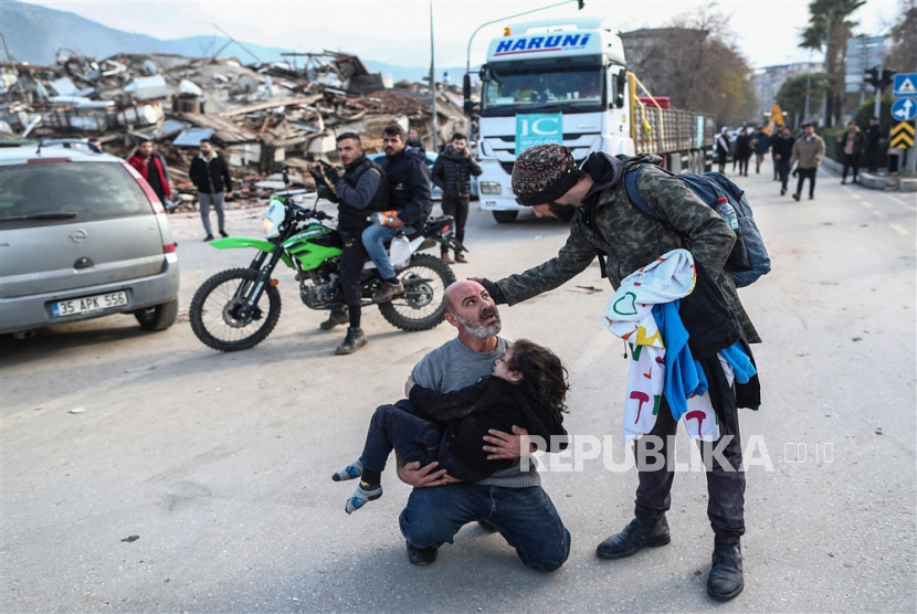  Seorang pria menggendong seorang gadis yang diselamatkan dari puing-puing bangunan yang runtuh di Hatay, Turki, Selasa (7/2/2023).  