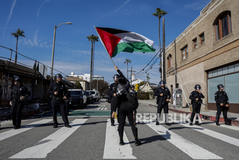 Seorang pengunjuk rasa mengibarkan bendera Palestina di depan petugas penegak hukum saat ratusan orang berdemonstrasi mendukung warga Palestina yang menyerukan gencatan senjata di Gaza dekat Teater Dolby tempat upacara Oscar Academy Awards ke-96 diadakan di bagian Hollywood dari Los Angeles, Ahad (10/3/2024).