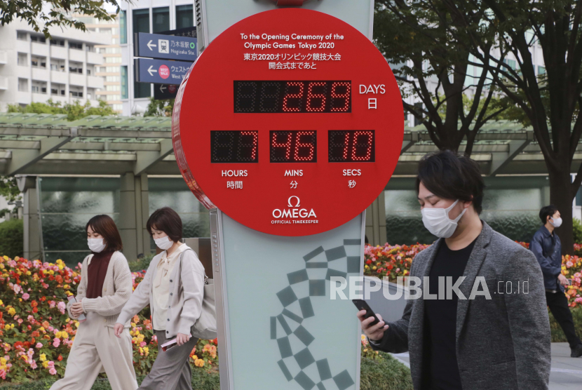 Orang-orang yang memakai masker wajah untuk melindungi dari penyebaran virus corona berjalan di depan jam hitung mundur menuju Olimpiade Tokyo di Tokyo, Selasa, 27 Oktober 2020.