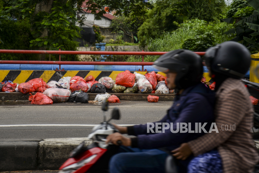 Pengendara motor melintas di dekat sampah yang dibuang di pinggir jalan (ilustrasi)