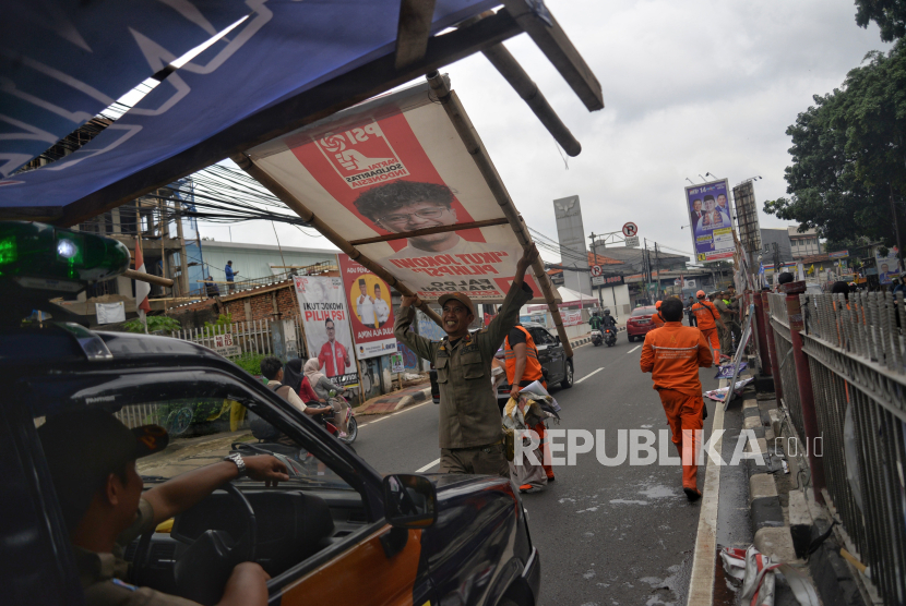 Petugas Satpol PP menertibkan alat peraga kampanye (APK) yang berada di pembatas jalan di Jalan Raya Bogor, Kramat Jati, Jakarta, Senin (29/1/2023).