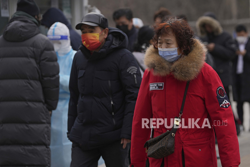 Orang-orang yang memakai masker wajah untuk melindungi diri dari virus corona berjalan oleh warga yang antre untuk diuji di fasilitas pengujian virus corona seluler di daerah perumahan di Beijing.