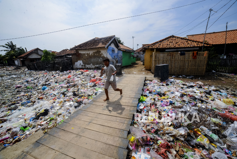 Seorang anak melintasi jembatan di sekitar tumpukan sampah di kali Peng, Tirtayasa, Kabupaten Serang, Banten, Rabu (10/7/2024). 