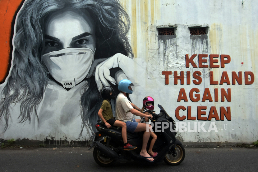 Warga negara asing melintas di dekat mural bergambar perempuan menggunakan masker di Badung, Bali, Minggu (24/1/2021). Jumlah kasus positif COVID-19 di Bali meningkat saat Pemberlakuan Pembatasan Kegiatan Masyarakat (PPKM). 
