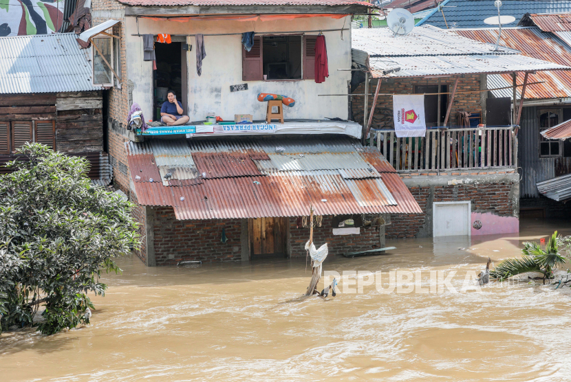  Seorang wanita duduk di lantai dua rumahnya di daerah permukiman yang banjir di Medan, Sumatera Utara (ilustrasi)