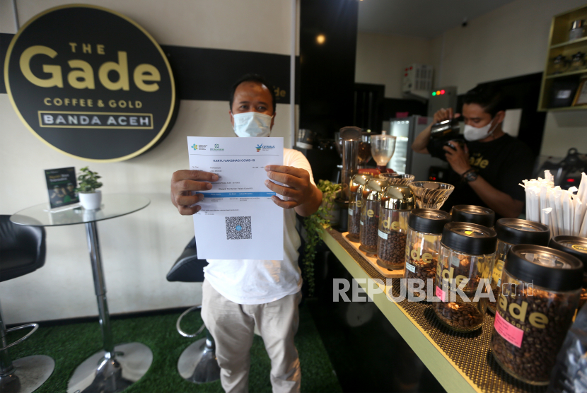 Pengunjung salah satu warung kopi (warkop) memperlihatkan sertifikat vaksin COVID-19 seusai mendapatkan suntikan yang digelar Polda Aceh di Banda Aceh, Aceh, Minggu (10/10/2021). Polda Aceh bekerja sama dengan pengusaha cafe dan restoran untuk menggelar vaksinasi dari warkop ke warkop sebagai upaya mensosialisasikan vaksin serta memutus rantai penyebaran dan penularan COVID-19. 
