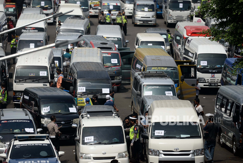 Polisi dan pengemudi beraktivitas didepan mobil travel gelap yang terjaring dalam operasi khusus di titk penyekatan di Polda Metro Jaya, Jakarta