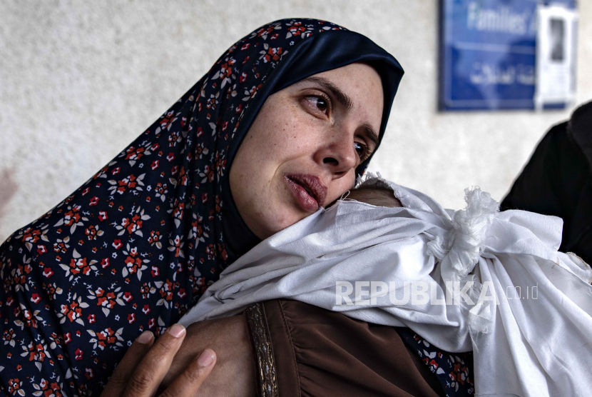 Seorang ibu dari anak perempuan kembar yang berduka, bagian dari keluarga Palestina yang terbunuh setelah serangan udara Israel yang menewaskan 14 orang, menggendong tubuh mereka yang terbungkus. 